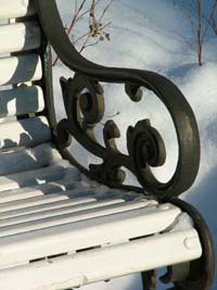 Park bench with wrought -iron handles on a snowy day.