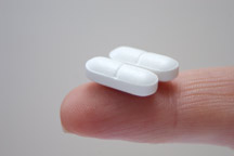 Two white capsule pills sitting on the tip of someone's index finger.